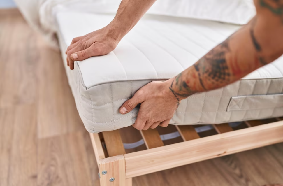 man holding mattress over the box spring in the bedroom with wooden floor