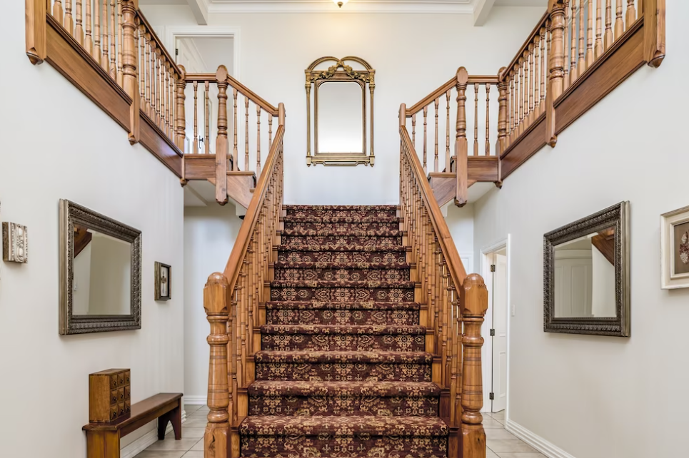 wooden staircase with a vintage carpet inside an apartment with white walls and small mirrors